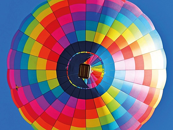 the view from looking directly up at a colourful hot air balloon on a blue sky